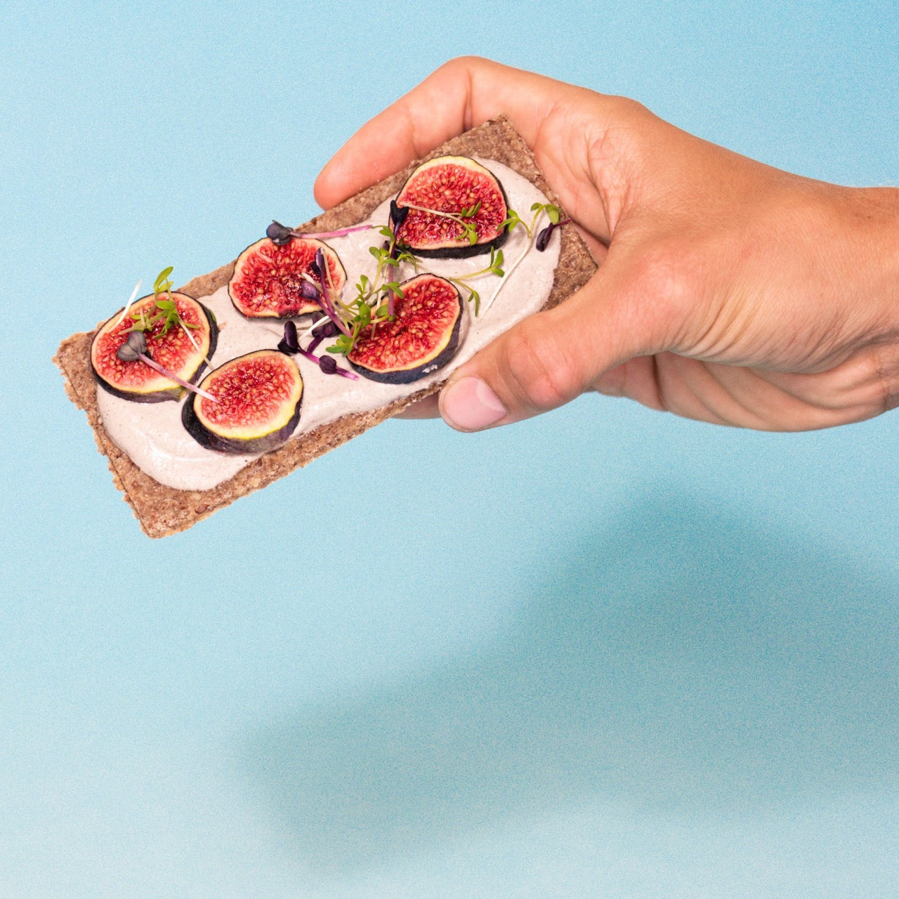 Eine Hand hält eine Scheibe Essener Rohkostbrot mit Feigen und Kresse belegt.
